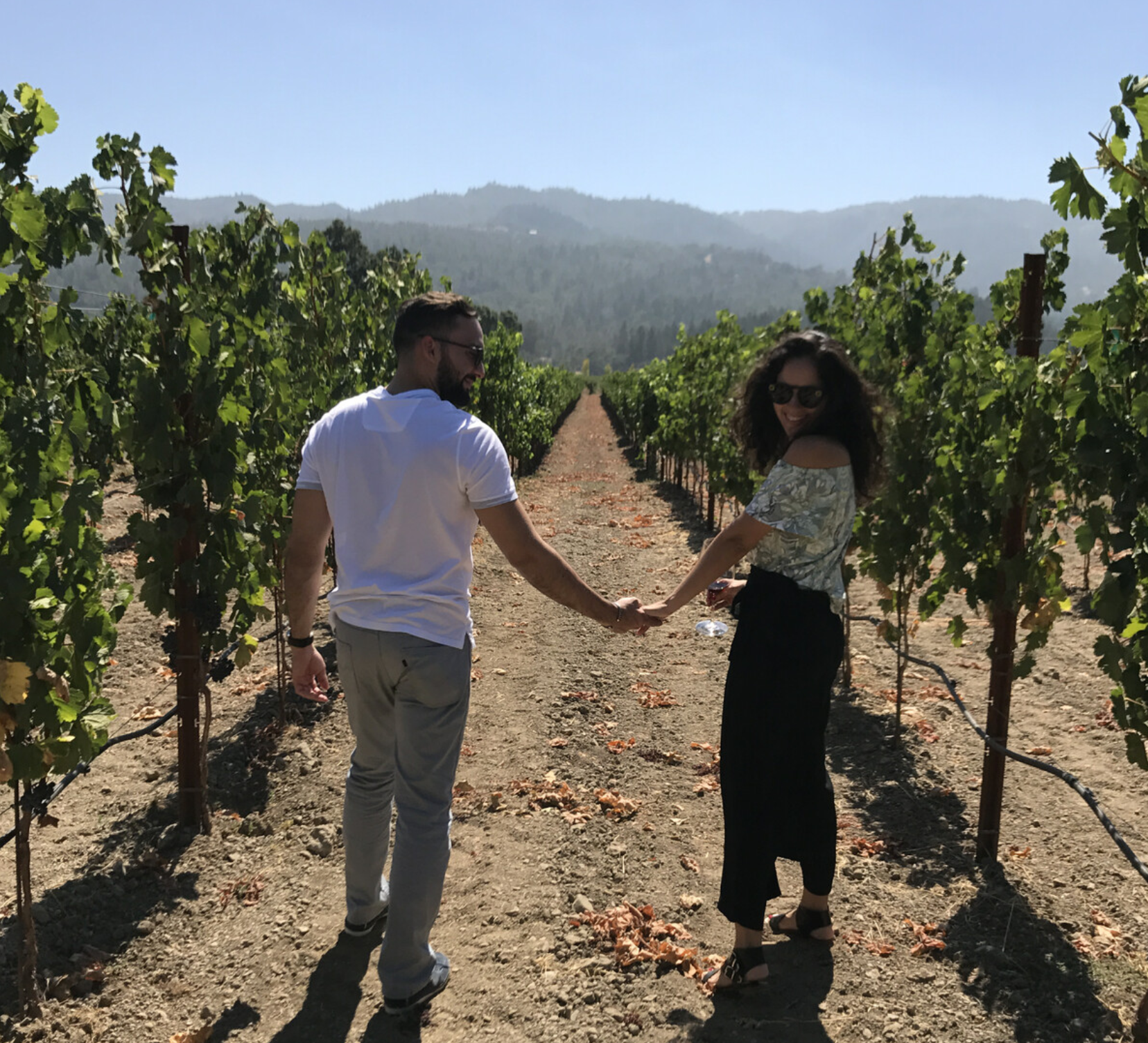 Andrés y Jahaira tomados de la mano entre las hileras de un viñedo.